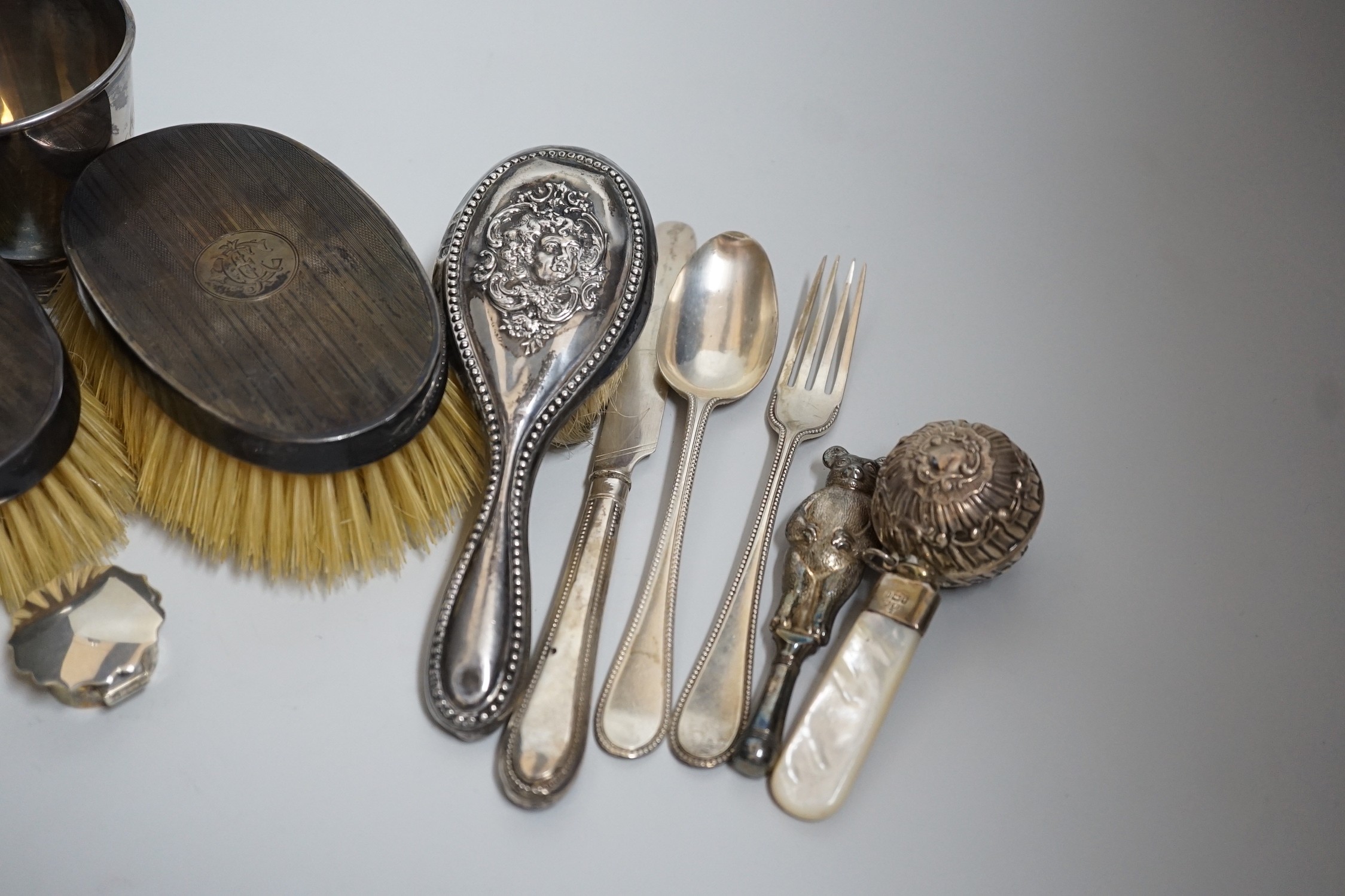 A mixed group of silverware including a pair of silver mounted clothes brushes, two rattles, a napkin ring, a christening trio and mug.